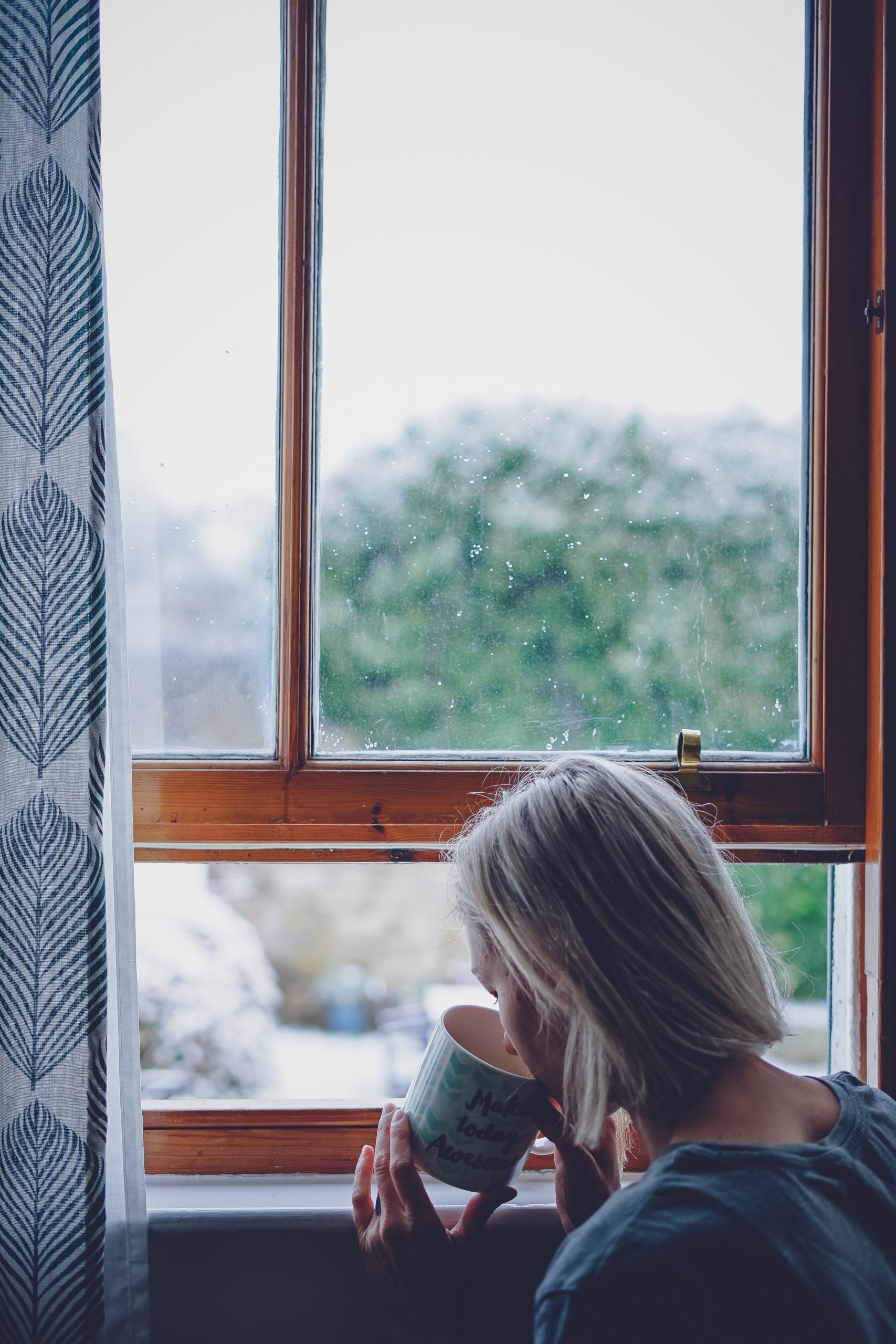 woman drinking in front of window at daytime